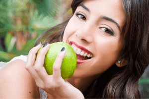 A woman eating a fruit while keeping her teeth white.
