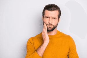 An image of a man holding his cheek due to wisdom tooth pain
