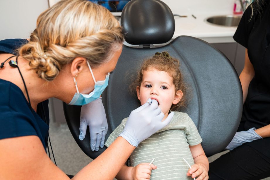 Emergency dental assistance for children A photograph of a dentist performing a dental examination on a young girl's teeth.