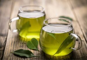 A cup of green tea with fresh leaves on a rustic wooden table.